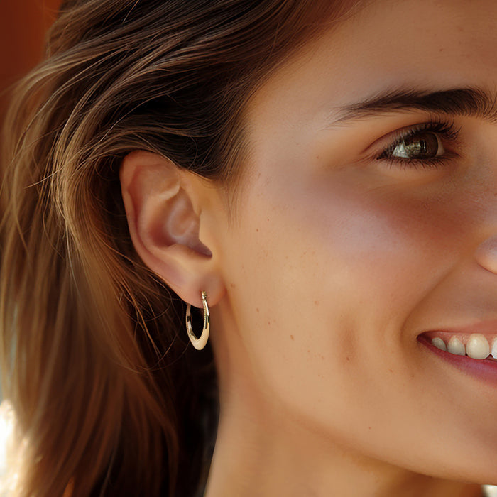 Gold beaded hoop earrings on a model's ear, small rounded hoops