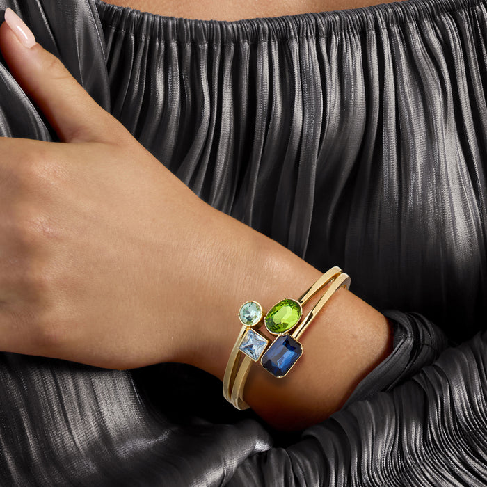 Gold-plated bangle bracelet on wrist with blue and green simulated gemstones