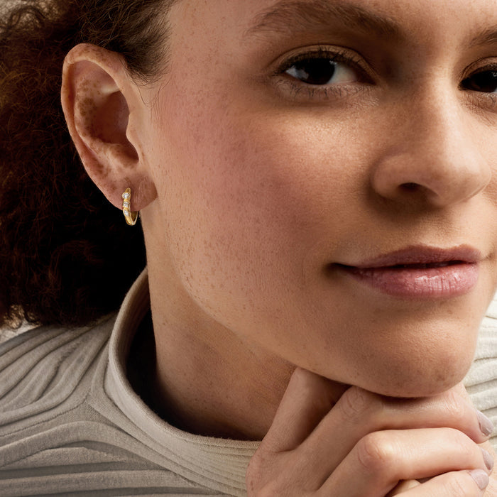 Gold hoop earrings with small round diamond accents worn on ear.
