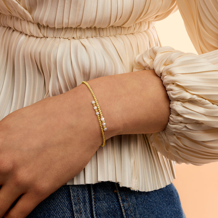Pearl beaded bypass cuff bracelet on wrist, white cultured pearls with yellow gold beads