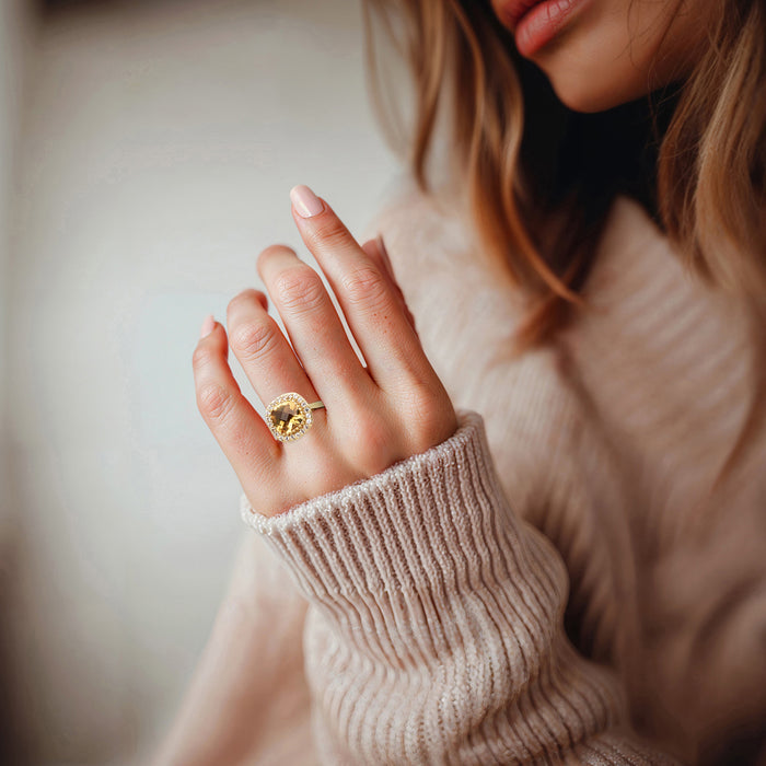 Gold ring with oval yellow gemstone and white topaz halo worn on hand