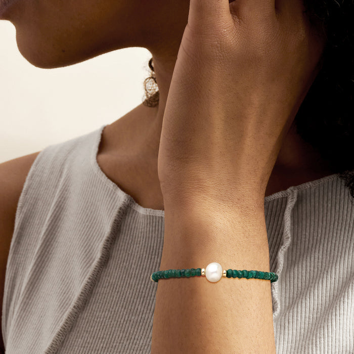 Green bead bracelet on wrist with white pearl centerpiece and yellow gold clasp