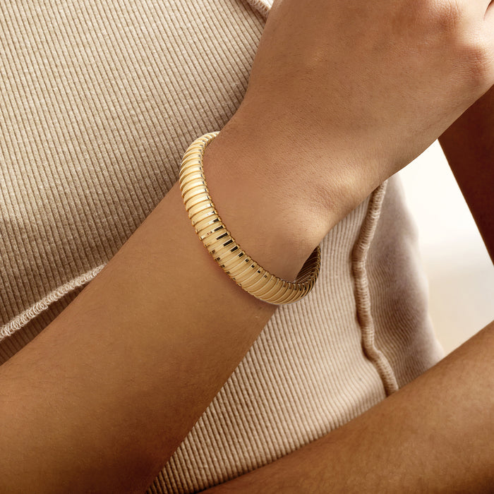 Yellow gold-plated tubogas cuff bracelet on wrist, ribbed tube texture
