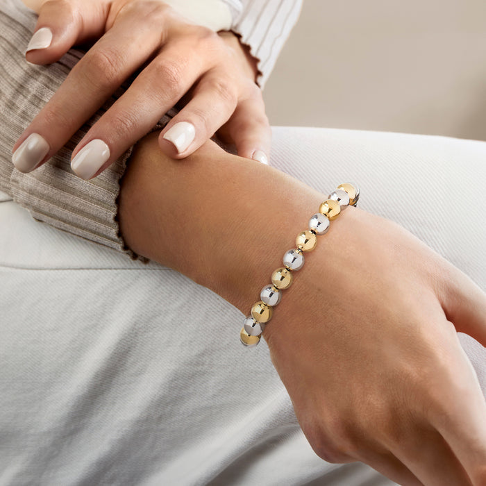 Beaded bracelet on wrist, alternating gold and silver round beads with chain clasp