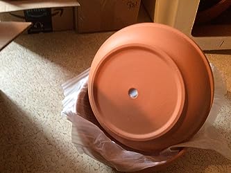 A terra cotta cactus and succulent pot with drainage holes sits upside-down on plastic wrap, surrounded by boxes on a beige carpet.